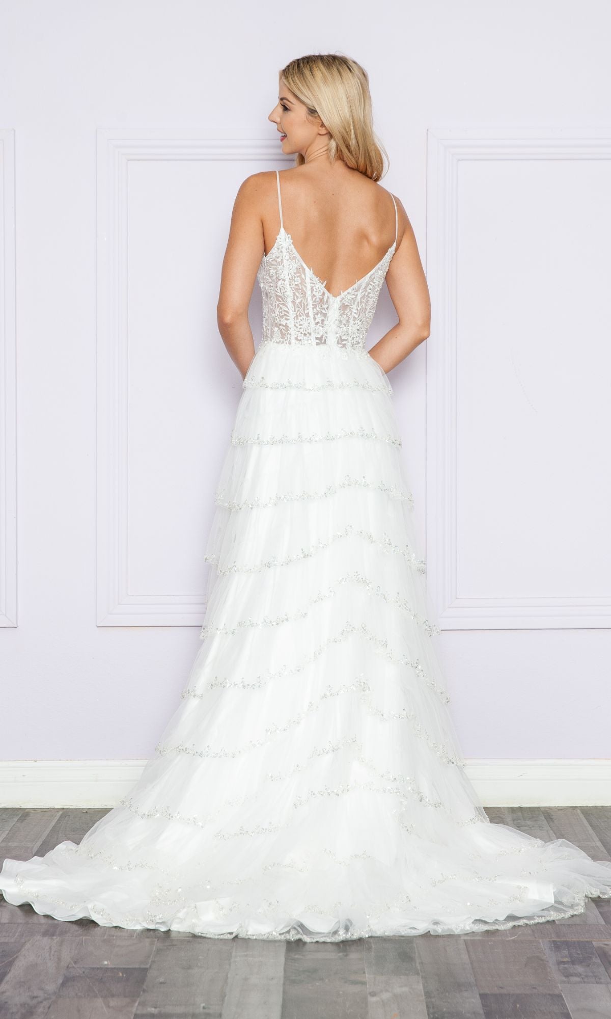 Woman wearing the Ruffled Long A-Line Tiered Prom Dress: Poly 9404, featuring an embroidered v-neck bodice and a tiered, ruffled skirt, shown from the back against a light-colored wall.